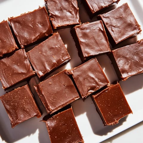 A close-up of glossy, dark chocolate fudge showing its smooth, creamy texture and perfect squares.