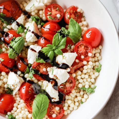 A close-up of Caprese Couscous Salad in a white bowl, featuring tender Israeli couscous mixed with halved cherry tomatoes and creamy mozzarella pearls.  