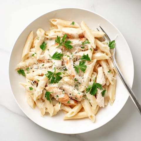 Fork-tender penne pasta coated in a rich roasted garlic cream sauce with juicy slices of roasted chicken breast and fresh parsley garnish.