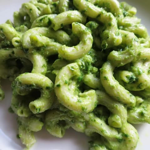 A fork twirls tender pasta coated in luscious avocado pesto sauce, highlighting the bright green, creamy texture and fresh, zesty aroma of this satisfying vegetarian main.