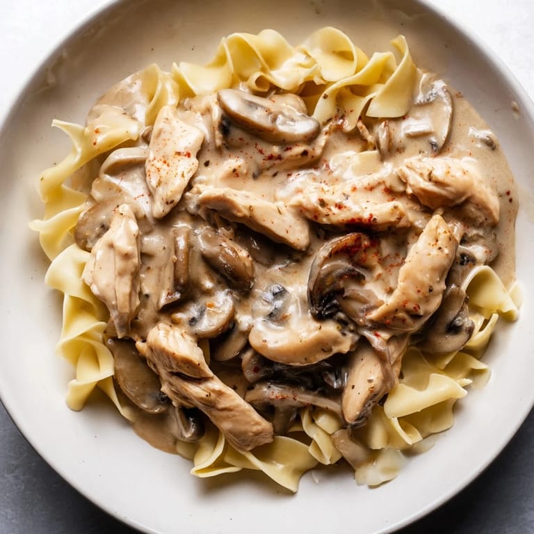 A close-up of creamy Chicken and Mushroom Stroganoff, featuring golden chicken and sautéed mushrooms on a bed of fluffy egg noodles.  