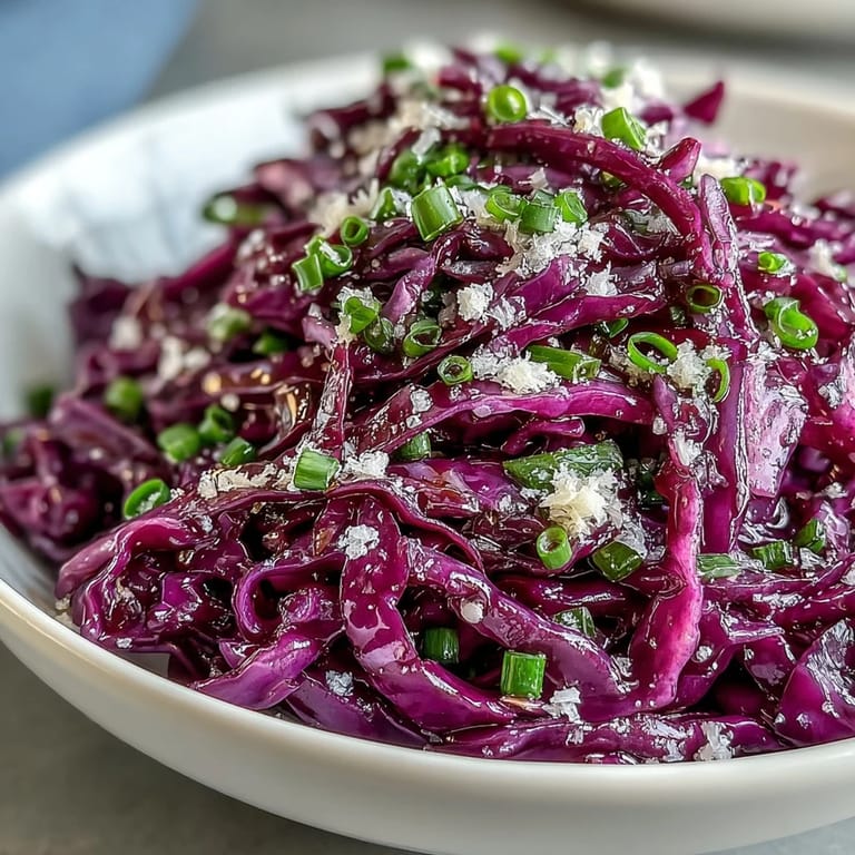 Shredded Red Cabbage Coleslaw With Apple and Parmesan served in a white bowl, topped with shaved cheese and fresh parsley.