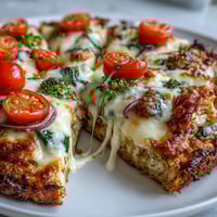 A close-up of Broccoli Chicken Crust Pizza, featuring a golden, crispy base topped with melted mozzarella, vibrant red bell peppers, and fresh spinach leaves.