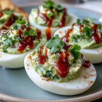 Creamy avocado deviled eggs topped with a spicy Sriracha drizzle, perfect for parties or a healthy snack.