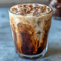 Starbucks Iced Brown Sugar Oat Milk Shaken Espresso in a tall glass with ice, oat milk, and a sprinkle of cinnamon on top.