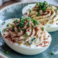 Classic deviled eggs with paprika and chives, creamy yolk filling piped into tender egg whites, topped with smoky spice and fresh herbs.